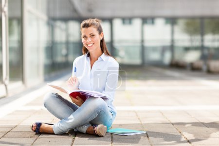 Brunette female student sitting on the floor with notebook