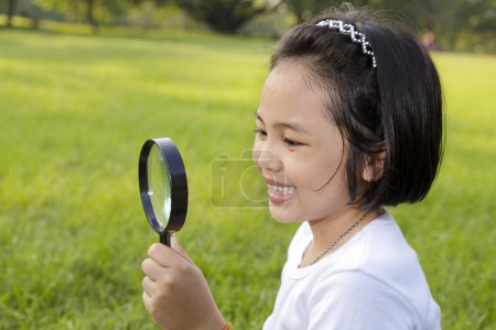 Asian little girl holding a magnifying glass in outdoor