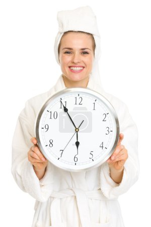 Young woman in bathrobe showing clock and thumbs up