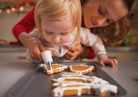 Baby helping mother decorate homemade christmas cookies with glaze