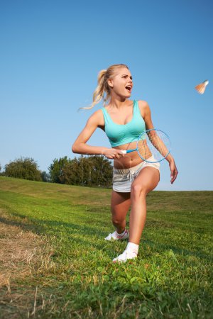 Fitness, young woman playing badminton in a city park