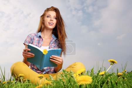 Woman on green field reading book