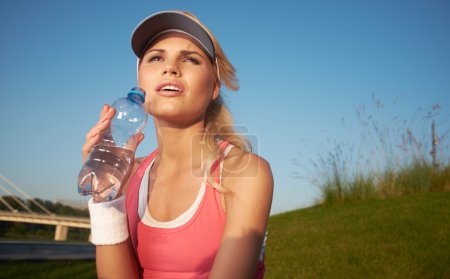 Woman drinking water after doing sports outdoors