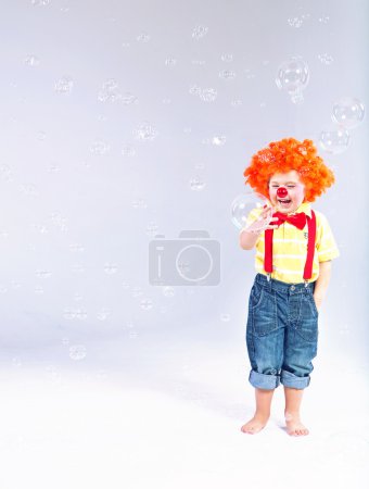 Funny picture of little clown making huge soap bubbles