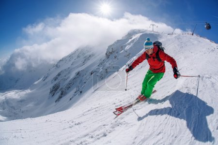 Skier skiing downhill in high mountains during sunny day