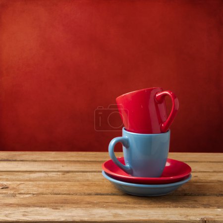 Red and blue coffee cups on wooden table over red grunge wall