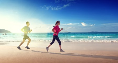 Man and women running on tropical beach at sunset 