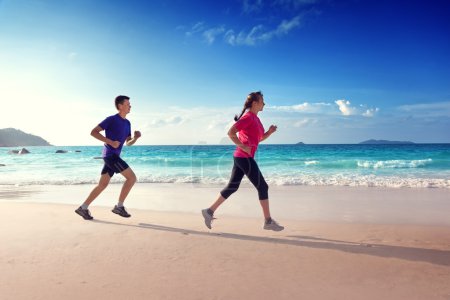 Man and women running on tropical beach at sunset 