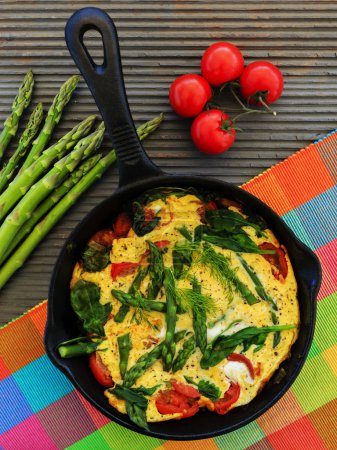 Omelette with asparagus and tomato on frying pan