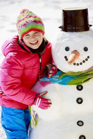 Winter fun, happy kid playing with snowman