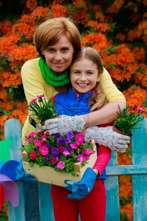 Gardening - lovely girl with mother working in flowers garden