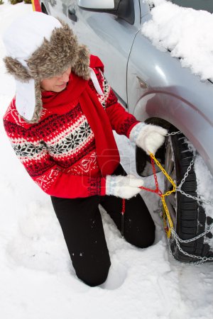 Winter, travel - woman putting snow chains onto tyre of car