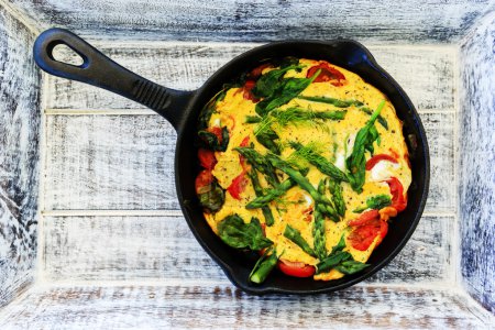 Omelette with asparagus and tomato on frying pan