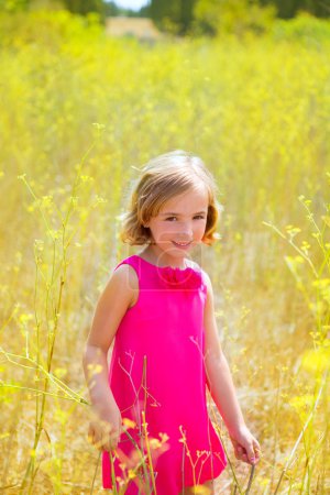 child kid girl in spring yellow flowers field and pink dress