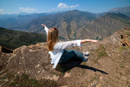 A girl sitting on a rock on a cliff in canyon, Dagestan
