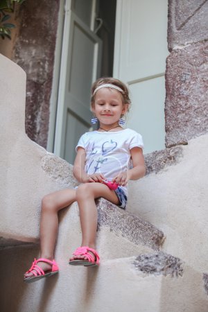 Adorable little girl sitting on the steps of old house in Emporio village, Santorini, Greece