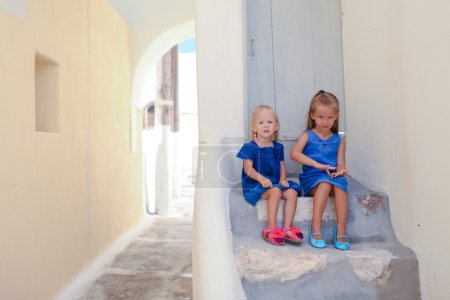 Two little adorable girls sitting on doorstep of old house in Emporio village, Santorini, Greece