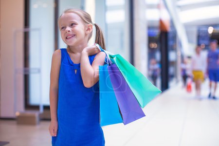 Little fashion girl with packages in a large shopping center