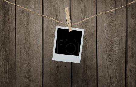 Blank photograph hanging clipped to the rope over wooden backgro