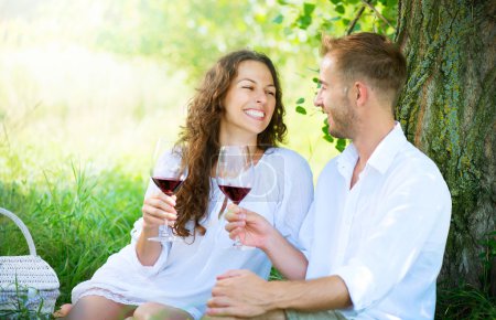 Picnic. Young Couple relaxing and drinking Wine in a Park