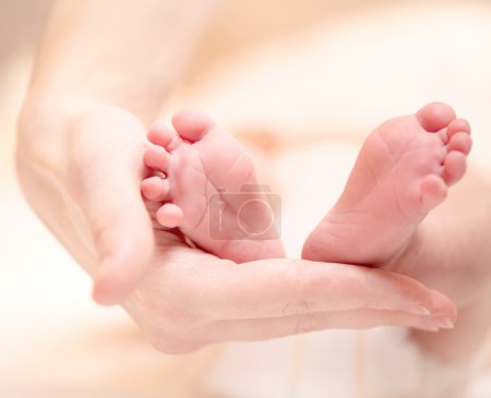 Tiny Newborn Baby's feet on female hands closeup