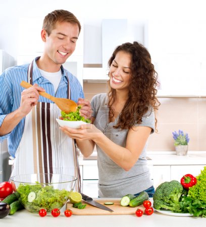 Young Man Cooking. Happy Couple Eating Fresh Vegetable Salad