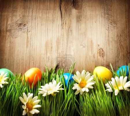 Colorful Easter Eggs in Spring Grass and Flowers over Wood