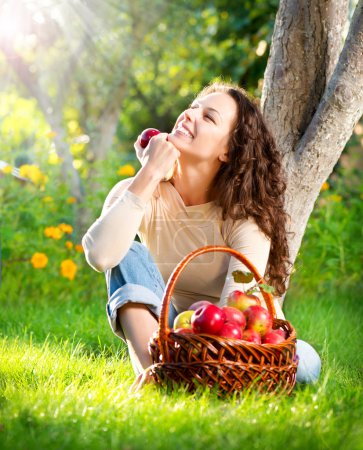 Happy Smiling Young Woman Eating Organic Apple in the Orchard