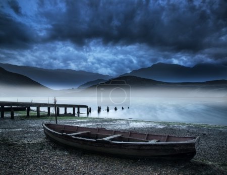 Old boat on lake of shore with misty lake and mountains landscap
