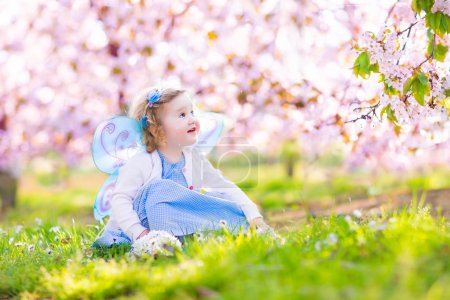 Curly toddler girl in fairy costume playing in fruit garden