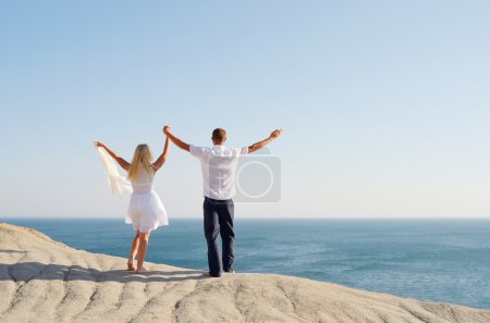 Young couple on a rock raised hands to the sky