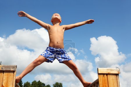 Boy in shorts standing on boards against clouds, plants hands an