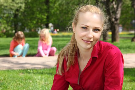 Beautiful blonde in park with playing children on background
