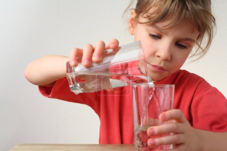 Little girl in red shirt pour out water from one glass to other,