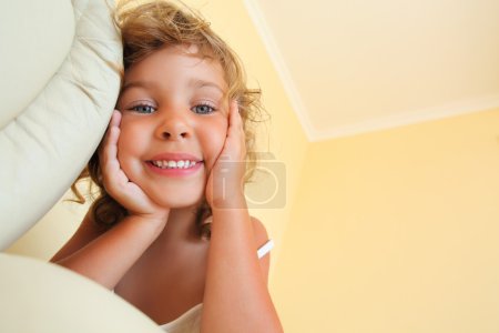 Pretty smiling little girl in cosy room, foreshortening from bel