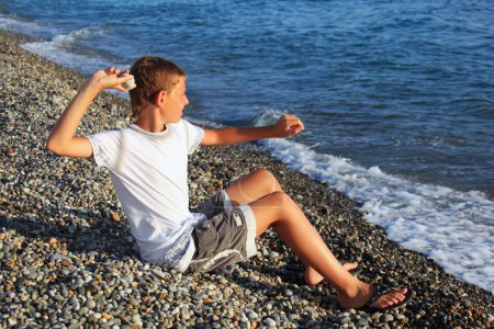Sitting boy throws stone in sea