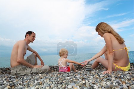 Parents with child on sea coast build pyramid of stones
