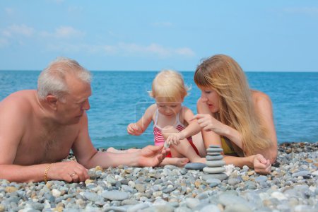 Mother and grandfather with child on sea coast and pyramid of s