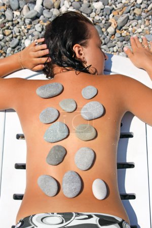 Beautiful woman sunbathes on beach with stones on back