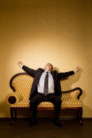 Businessman in suit stretches after dream sitting on sofa