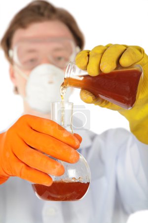 Scientist in respirator and rubber gloves pours brown liquid fr