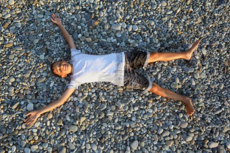 Teenager boy lying on stones on stone seacoast