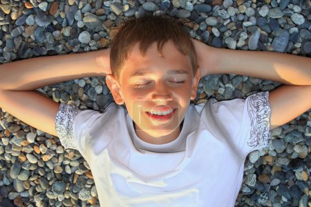 Teenager boy lying on stones on stone seacoast, closed eyes, hol