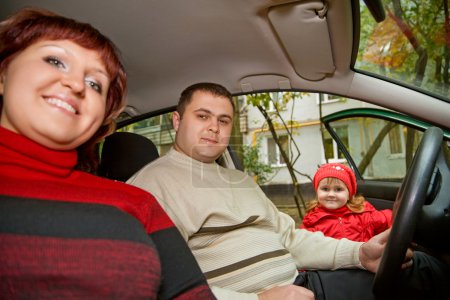 Married couple and little girl sit in car near a building