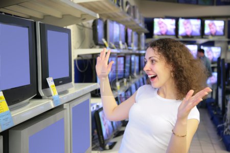 Young woman in delight looks at TVs in shop