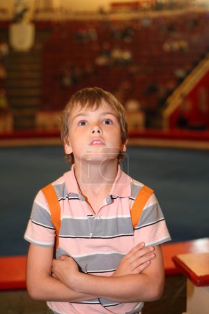Little boy in circus standing near arena and looking up half bod