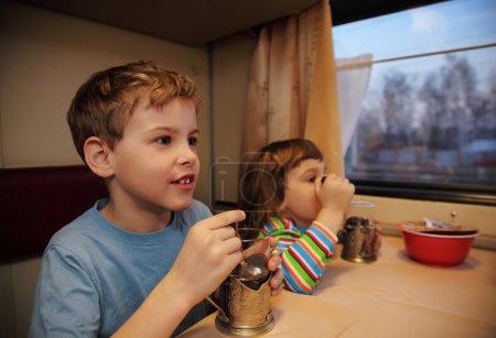Two children drink tea from glasses in train car