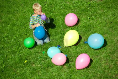The boy inflates balloons, sitting on a grass