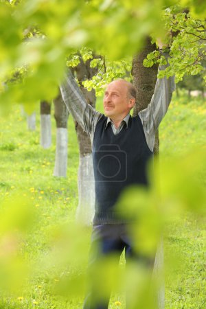 Mature smiling man with lifted hands in summer garden