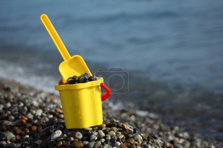 Yellow children's bucket full of pebble with scoop on seacoast